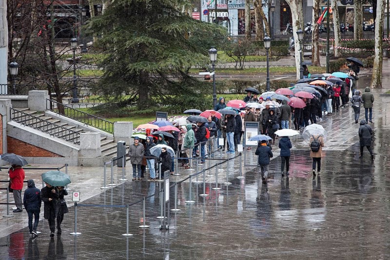 Tourists from abroad stand by the line with their umbrellas to get a ticket for a visit to the Prado Museum on a rainy sunday in Madrid