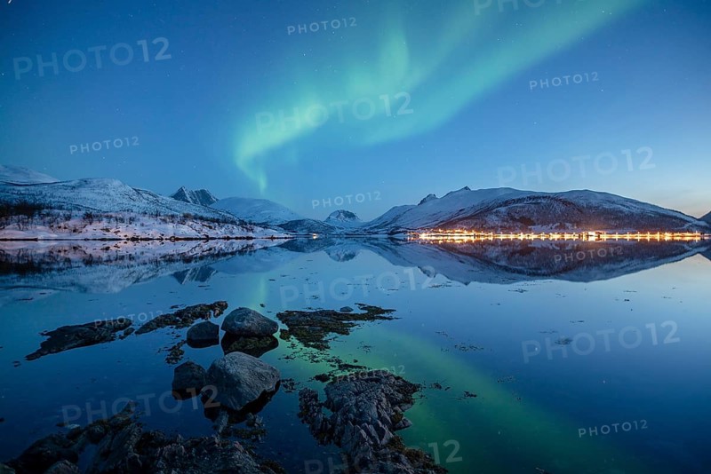 Aurora borealis above snow-capped peaks reflected in a fjord