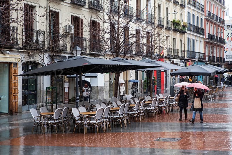 Empy seats in terraces of chueca square in the gay district as people walks by on a rainy day