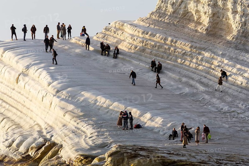 Tourists hiking on chalk cliffs Scala dei Turchi in the evening