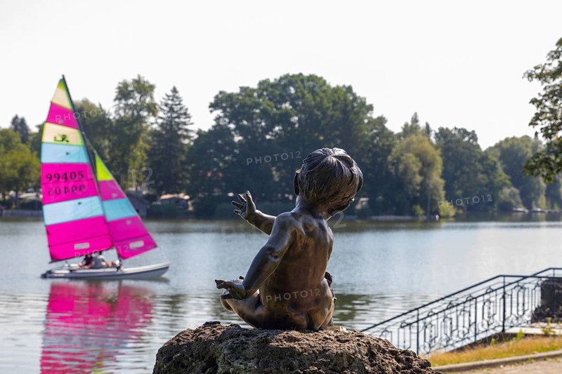Statue on the beach promenade at Waginger See with sailing boat