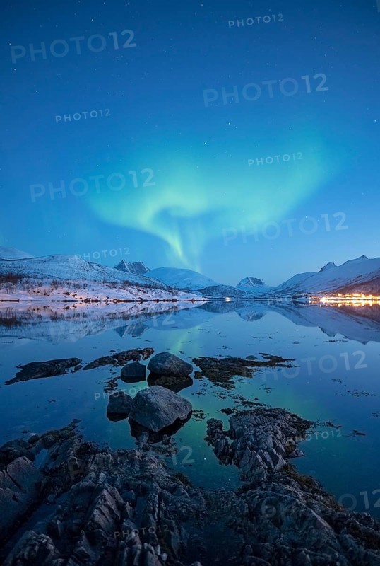 Aurora borealis above snow-covered peaks reflected in a fjord