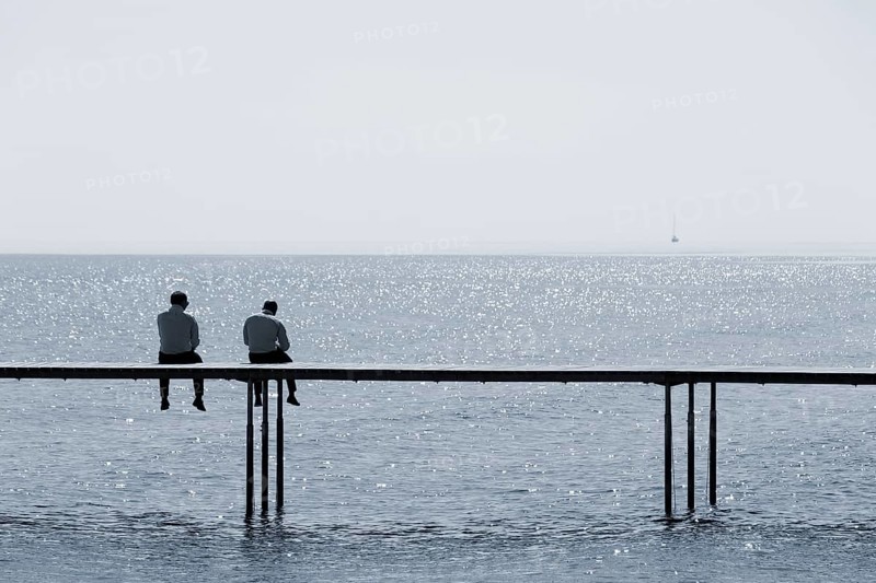 Two men sitting on a bathing jetty by the sea