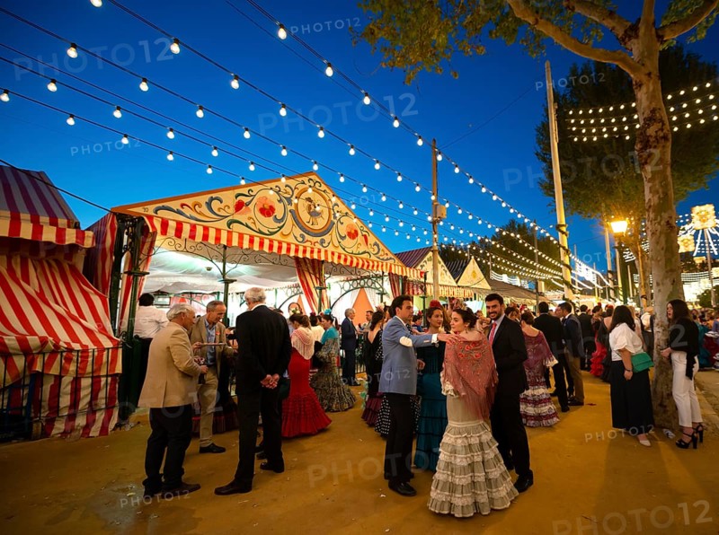 Spaniards celebrating in traditional clothes in front of lit marquees