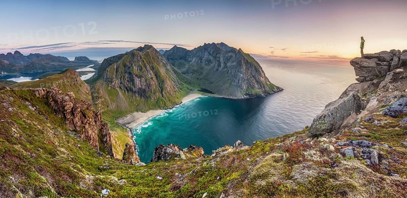 Tiny person on rocky outcrop overlooks Kvalvika beach and wide sea