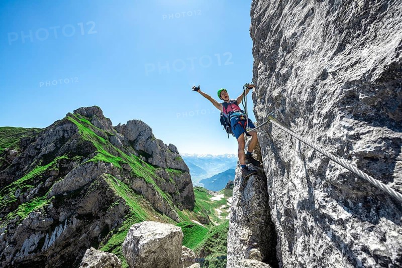 Young man stretching his arms in the air while climbing a rock face