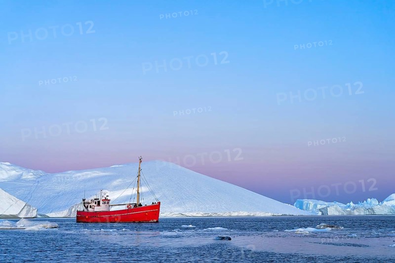 Red boat with tourists in front of icebergs at the blue hour