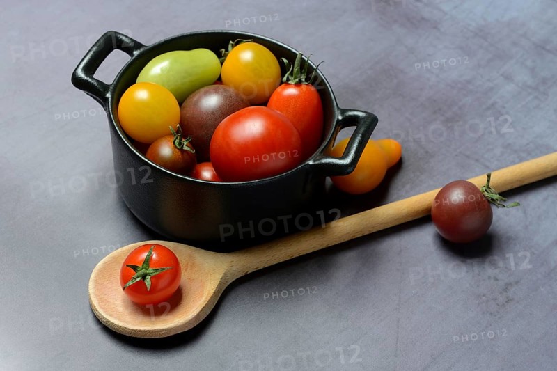 Different cherry tomatoes in pot with cooking spoon