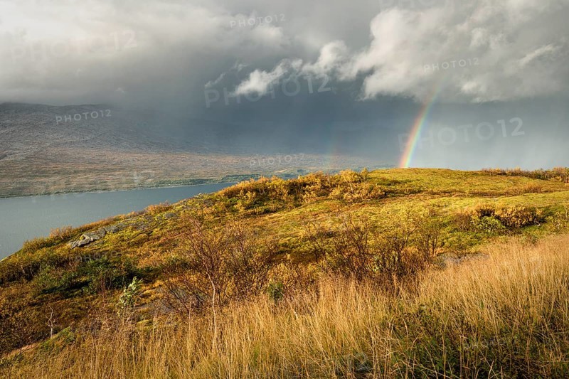 Thunderstorm with double rainbow and dramatic clouds with yellow grass on hills in autumn