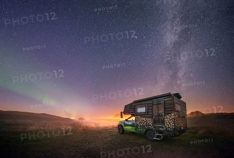 Night shot of a painted camper van under the Milky Way with northern lights