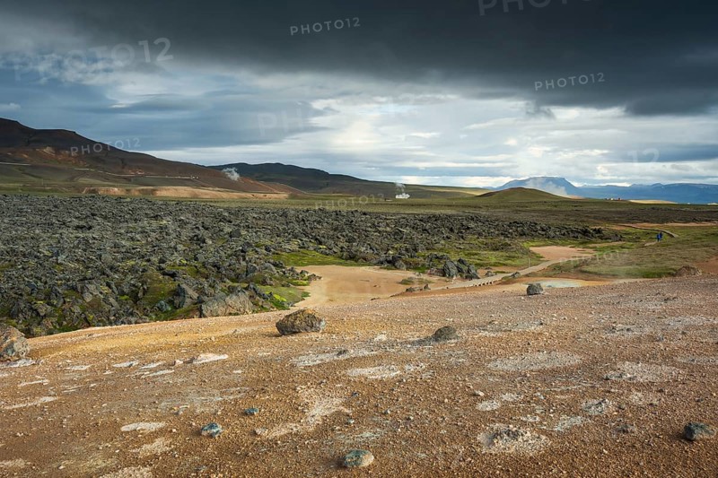Black lava flow in Krafla lava field with geothermal power plant in the distance