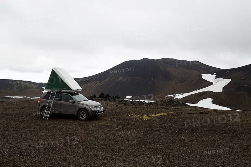 Off-road vehicle with roof tent and ladder on barren plateau