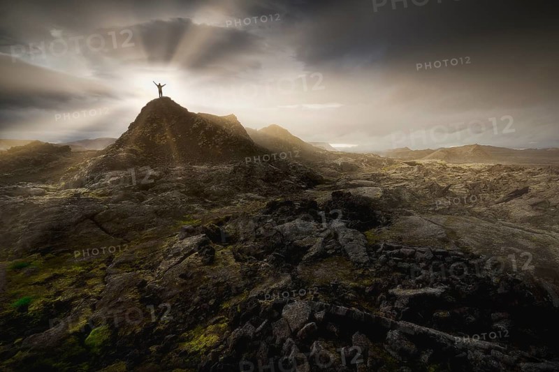 Man on a hill in a black lava field with green moss stretching hands into the dramatic sky