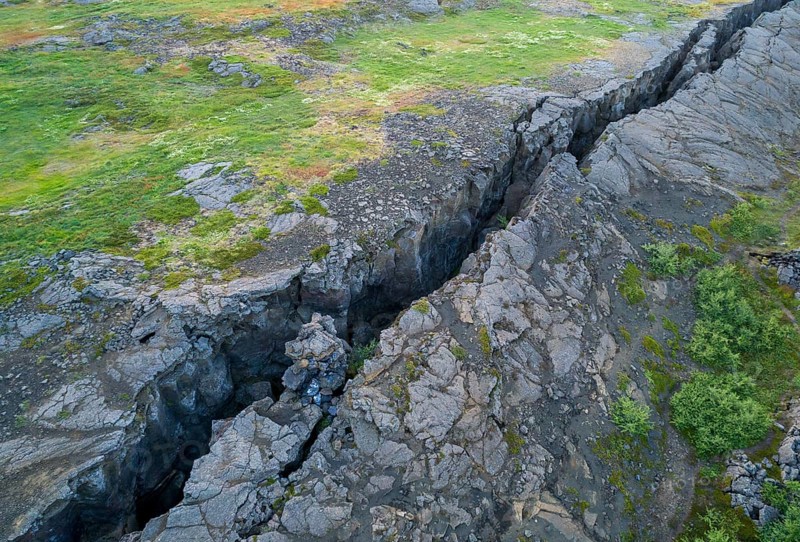 Black fissure runs through green meadow in fault zone