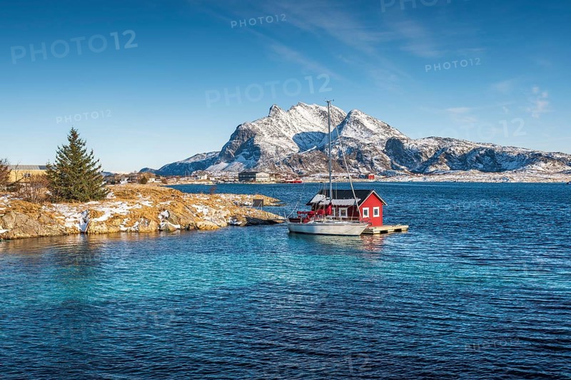 Red wooden cabin on raft with sailing boat in the sea off the coast