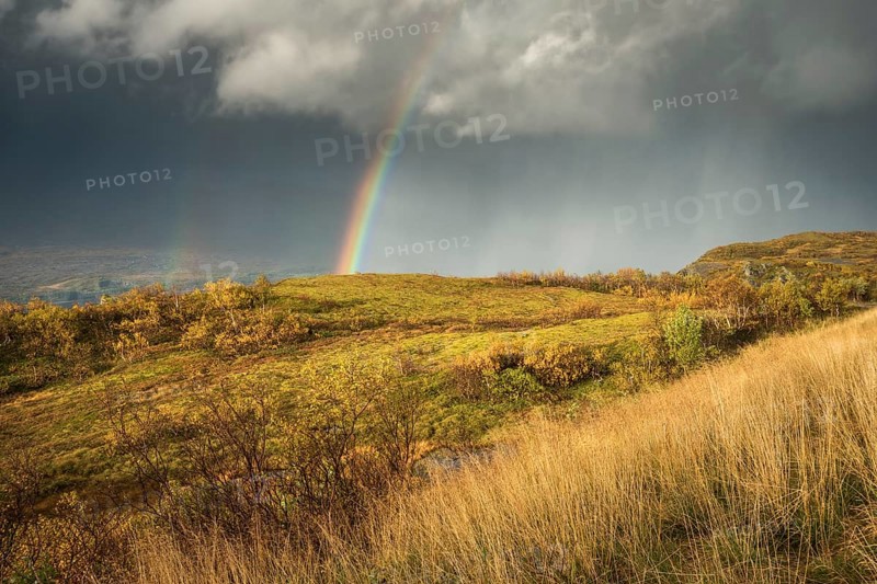 Thunderstorm with double rainbow and dramatic clouds with yellow grass on hills in autumn