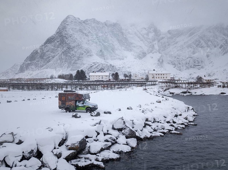 Motorhome painted as a mountain hut in snowfall at the parking lot in front of a fjord