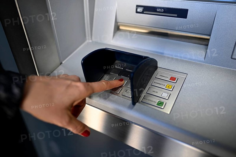 Woman typing in secret code at the cash machine of a savings bank