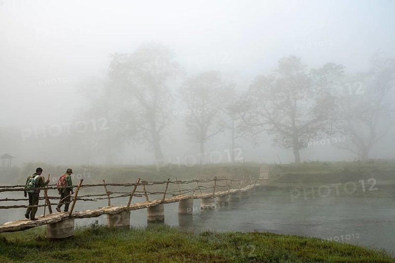 Two men walk in the morning fog over a bridge over the Rapti River