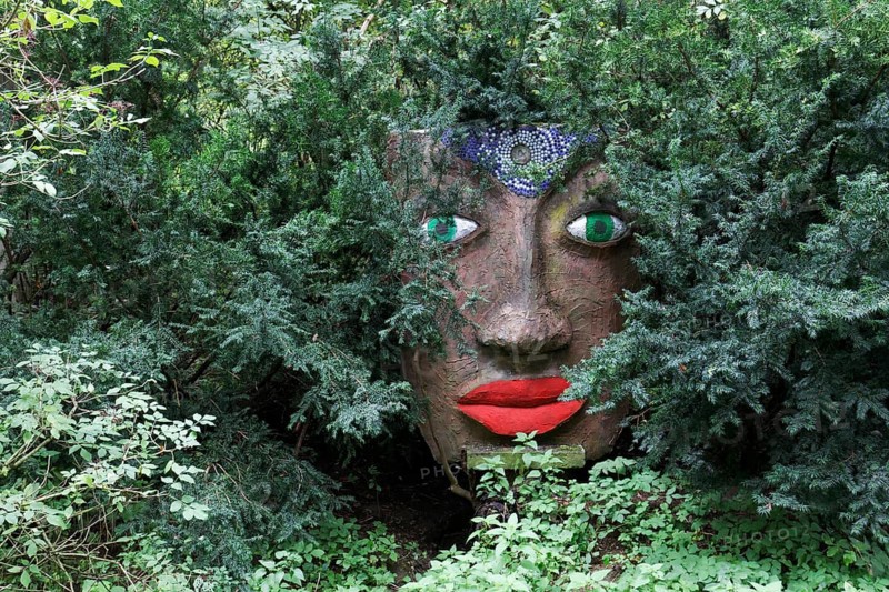 Magical woman face with red lips and green eyes looks through branches