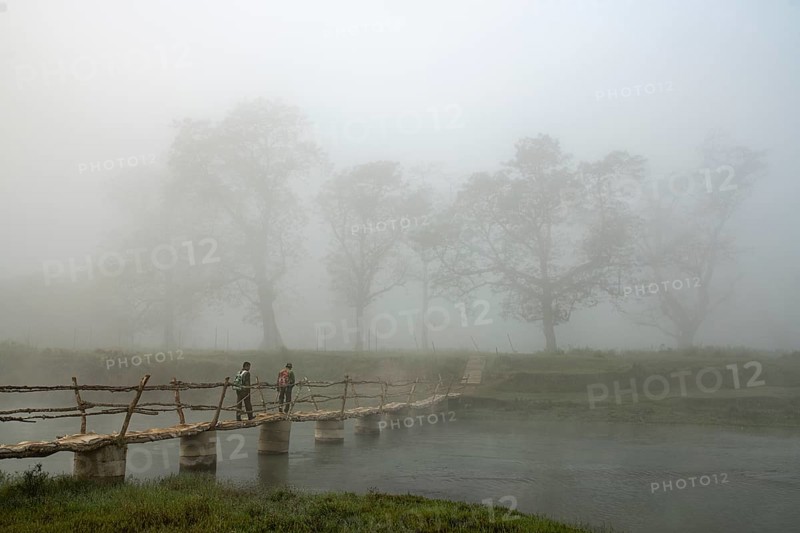 Two men walk in the morning fog over a bridge over the Rapti River
