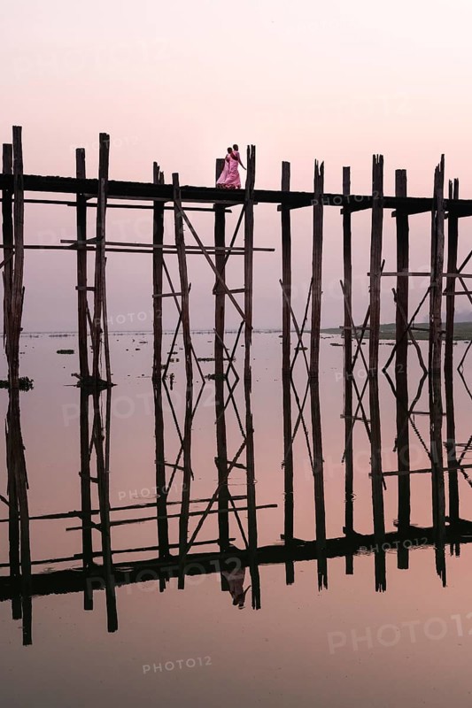 Buddhist monks walk across the U-leg bridge in pink robes as the sun rises