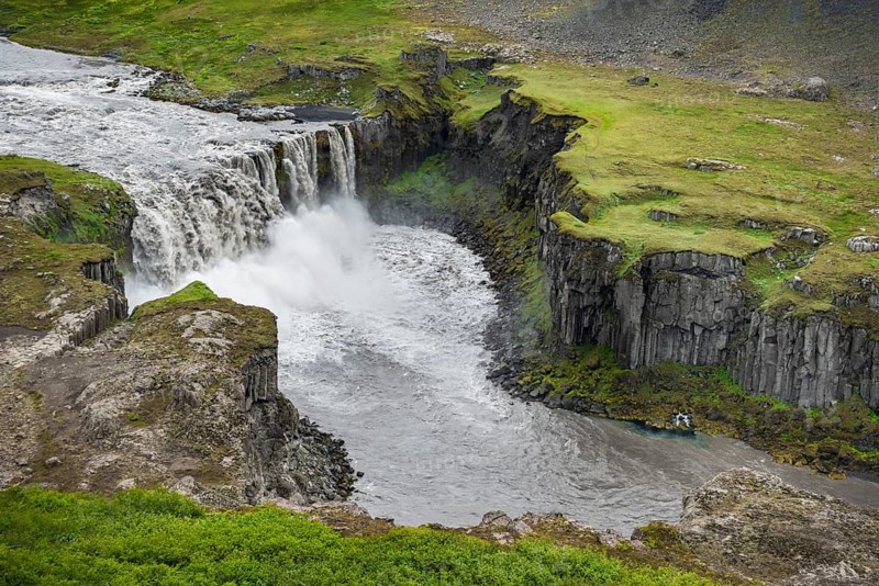 Waterfall falls from green volcanic plain over basalt columns into a canyon