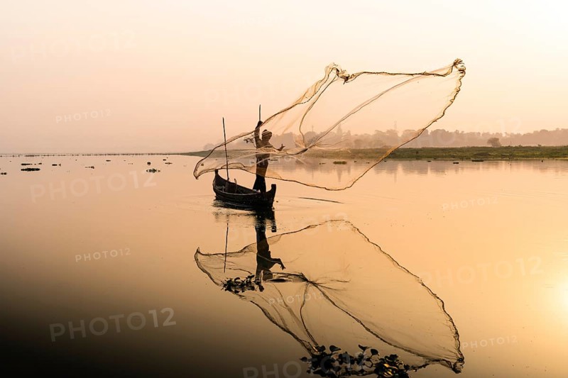 Fisherman with boat on Taung Tha Man Lake casts a fishing net for sunrise