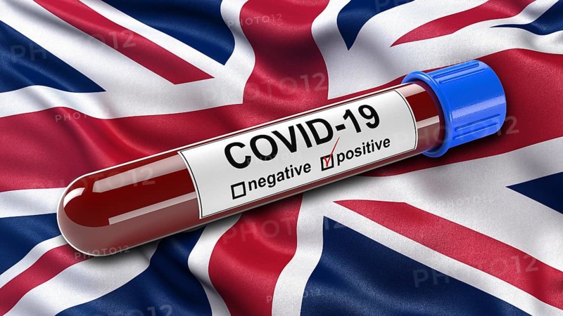 Flag of the United Kingdom waving in the wind with a positive Covid-19 blood test tube. 3D illustration