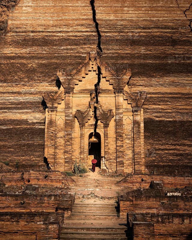 Buddhist monk stands with red umbrella in the entrance of Mingun Pagoda