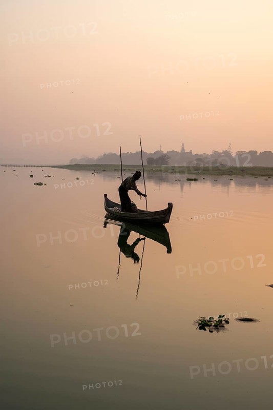 Fisherman stands with boat on the Taung Tha Man Lake to the sunrise