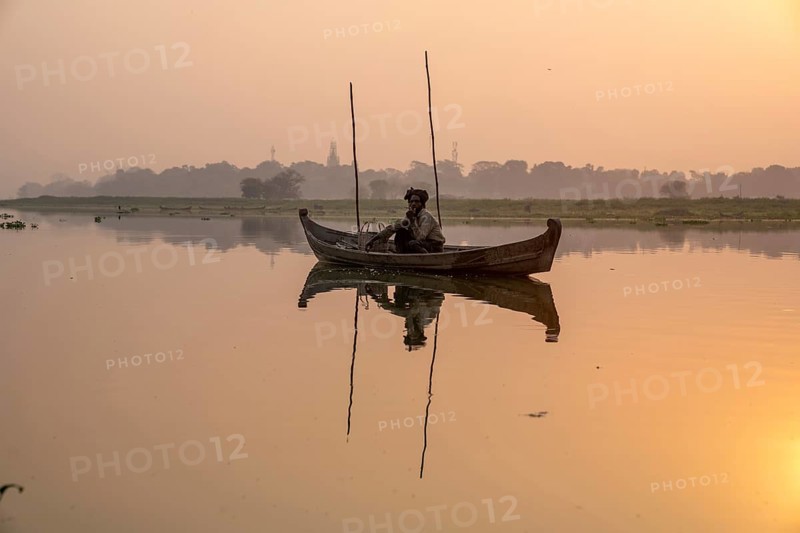 Fisherman sitting with boat on Taung Tha Man Lake at sunrise