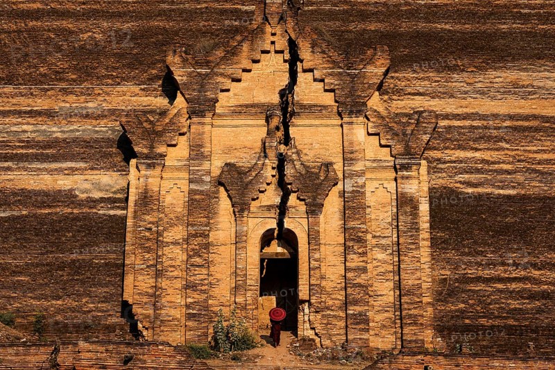 Buddhist monk stands with red umbrella in the entrance of Mingun Pagoda