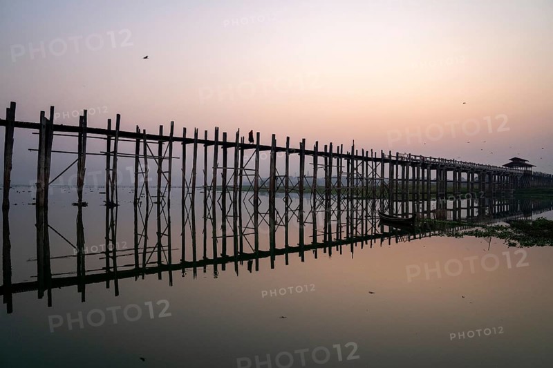 Buddhist monks walk across the U-leg bridge in red robes as the sun rises