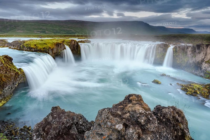 Long time exposure of a turquoise waterfall in volcanic landscape with dramatic clouds