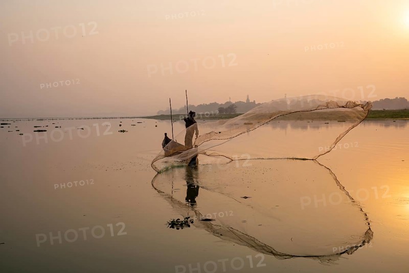 Fisherman with boat on Taung Tha Man Lake casts a fishing net for sunrise