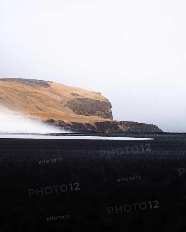 Yellow grassy mountain with black sand and waves in the foreground