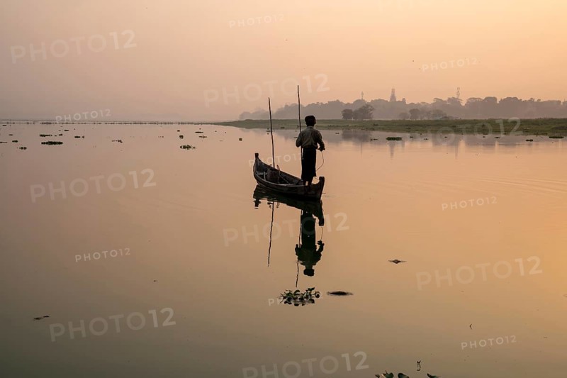 Fisherman stands with boat on the Taung Tha Man Lake to the sunrise