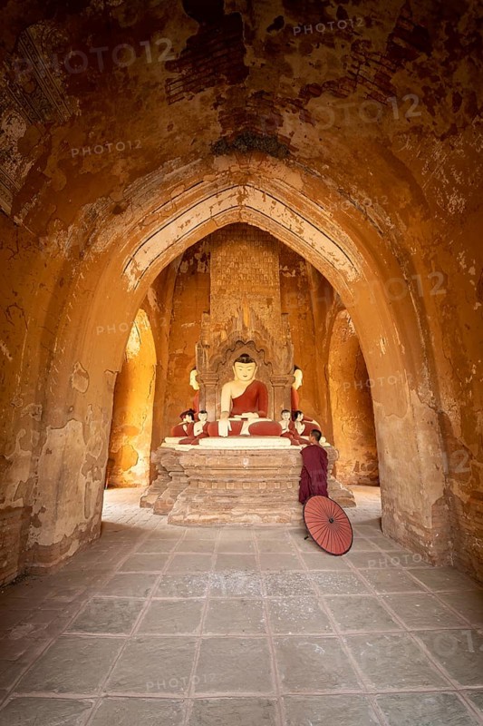 Buddhist young monk in red robe with red umbrella standing in a temple and praying