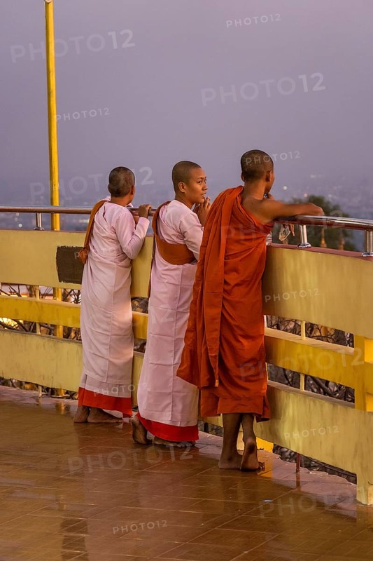 Three female Buddhist nuns at the railing of the Su Taung Pyae Pagoda