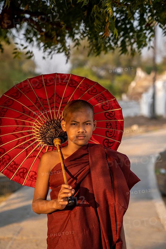 Buddhist monk stands with red umbrella on a path