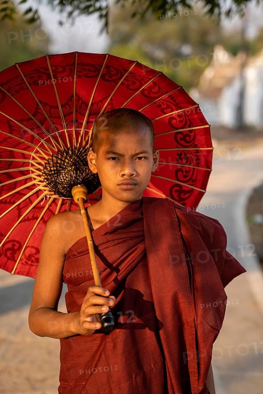 Buddhist monk stands with red umbrella on a path
