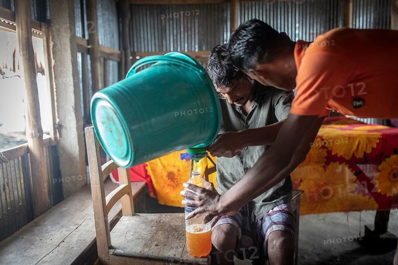 Honey collectors fill nectar from a bucket into plastic bottles