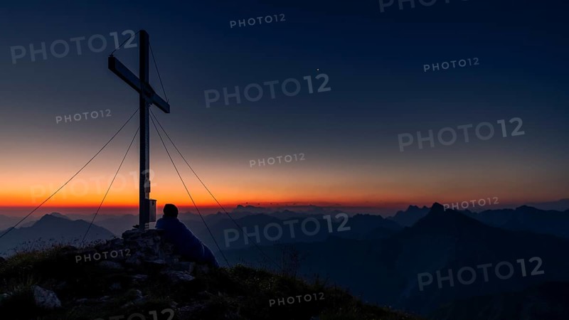 Cross of the Kreuzspitze at sunrise with mountaineer at the summit