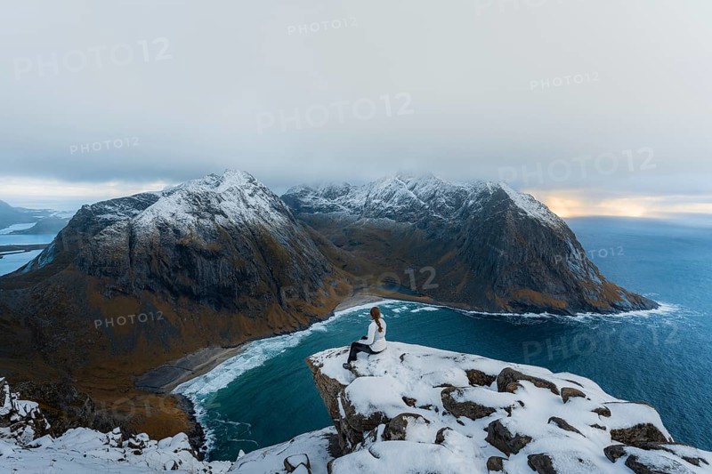 Woman sitting on a viewing platform on a mountain in front of Kvalvika beach