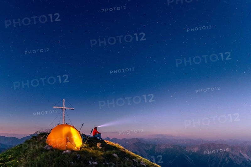 Cross of the Kreuzspitze by a starry sky with tent and mountaineer at the summit