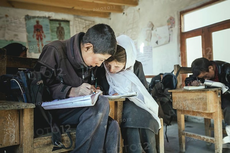 A boy and a girl writing in an exercise book on a school desk