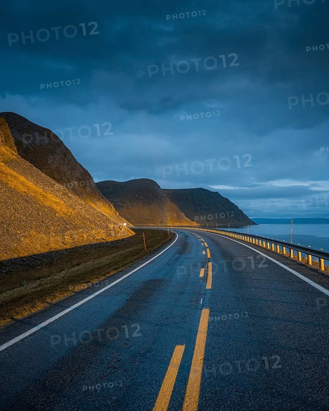 Road leading to rainbow with dramatic sky and sunset light