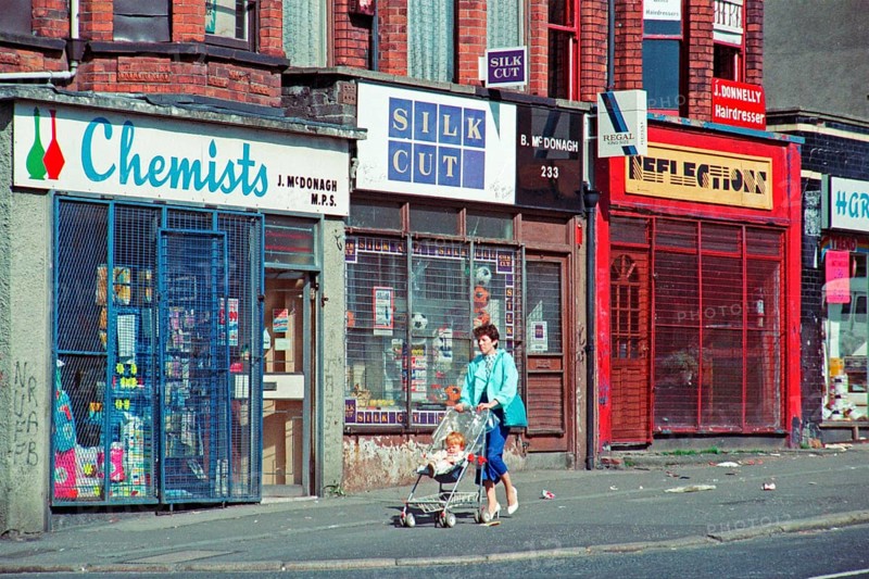 Woman with pram in front of barred shops