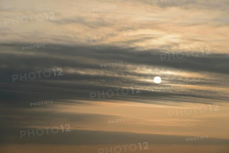 Sun shines behind layered clouds